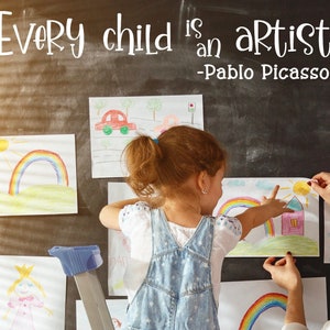 May include: A young girl and a woman are hanging up colorful drawings on a chalkboard wall. The drawings include a house, a rainbow, a car, and a sun. The quote "Every child is an artist. -Pablo Picasso- " is written on the chalkboard.