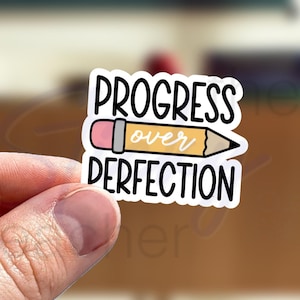 May include: A white sticker with a yellow pencil and the text "Progress over Perfection".