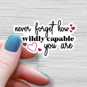 May include: White sticker with black text that reads "never forget how wildly capable you are" with pink hearts around the text.