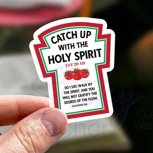 May include: A red and white sticker with the text "Catch Up With The Holy Spirit - Est 29 AD -" and a Bible verse from Galatians 5:16. The sticker is shaped like a ketchup bottle with a red cap and a red label. There are three red tomatoes on the label.
