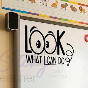 May include: A classroom whiteboard with the text "LOOK WHAT I CAN DO" in black. The words "CLASS GOALS" are in colorful letters above the board. A student job chart and colorful animal border are also visible.