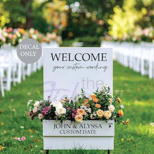May include: A white wooden welcome sign with the text "WELCOME" and "your custom wording". The sign has a floral arrangement at the base and includes the names "JOHN & ALYSSA" and a custom date.