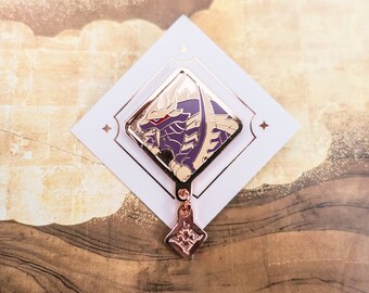 May include: A gold and purple enamel pin featuring a dragon-like creature with a detailed design. The pin is attached to a small, gold, diamond-shaped charm.
