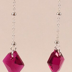 May include: A pair of dangle earrings with a silver chain and a deep pink faceted crystal pendant.