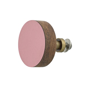 May include: A circular cabinet knob featuring a flat, matte pink front face attached to a cylindrical dark brown wooden base. The hardware includes a brass-toned metal stem, a small circular spacer, and a silver-colored metal screw with a washer.