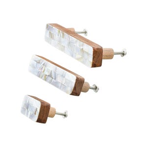 May include: Three rectangular cabinet knobs with a mosaic of white shell pieces set in a dark wood frame. The knobs have a light wood base and a silver screw for attachment. The knobs are in different sizes.