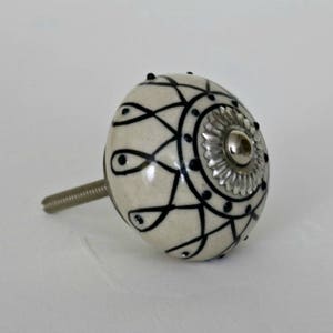 May include: White ceramic knob with a black and silver design. The knob has a screw on the back for attaching to a drawer or door.