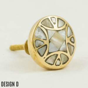 May include: A gold-toned cabinet knob with a circular design. The knob is decorated with a geometric pattern of white mother-of-pearl inlay.