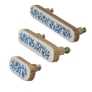 May include: Three oblong drawer pulls of varying lengths, each featuring a natural wood grain side profile and a white front face decorated with a blue floral vine pattern. Each pull includes a metal bolt and washer for mounting purposes.