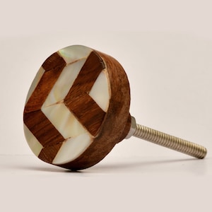 May include: A round wooden cabinet knob with a geometric pattern of white mother of pearl and brown wood. The knob has a silver metal screw.
