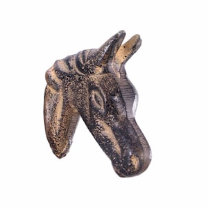 May include: A detailed, bronze-colored horse head sculpture. The sculpture has a textured surface with dark brown and tan hues. The horse head is angled slightly, showcasing the detailed features of the face and ears. The sculpture is set against a white background.