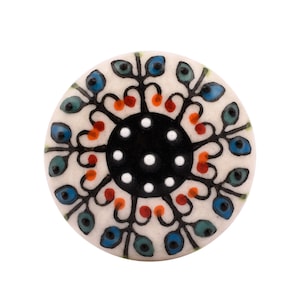 May include: A round ceramic knob with a white background and a black, white, and red floral design. The knob has a black center with white dots.
