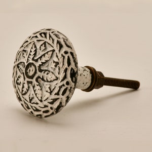 May include: White and black cast iron cabinet knob with a floral design. The knob has a screw on the back for attaching to a cabinet door.