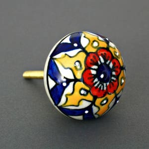 May include: A ceramic knob with a blue, yellow, red, and white floral design. The knob has a gold metal screw.