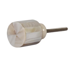 May include: A white and beige round cabinet knob with a silver screw. The knob is made of mother of pearl and has a geometric pattern.
