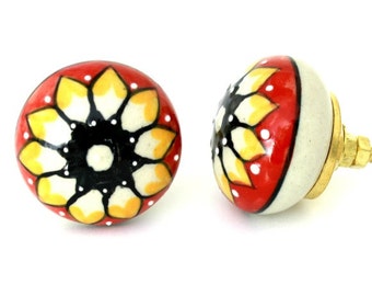 May include: Two ceramic cabinet knobs with a white base and a red, yellow, and black floral design.