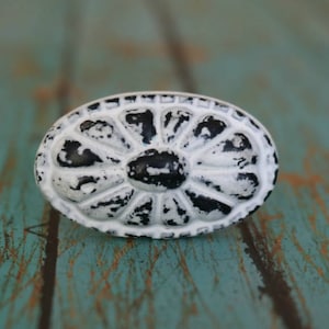 May include: White and black oval cabinet knob with a distressed finish. The knob has a raised floral design.