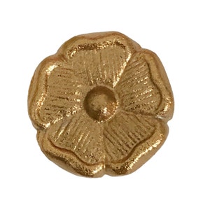 May include: A gold-colored metal flower-shaped knob with a raised center. The knob has a textured surface and a slightly rounded shape.