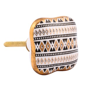 May include: White ceramic cabinet knob with a black and gold geometric pattern. The knob has a gold trim and a brass screw.