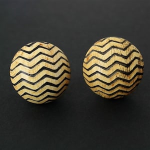 May include: A pair of round, wooden earrings with a black and white chevron pattern.