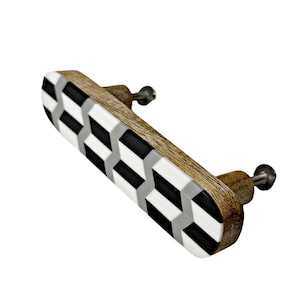 May include: A wooden cabinet pull with a geometric pattern in black, white, and gray. The pull has a rectangular shape and is attached to two screws.
