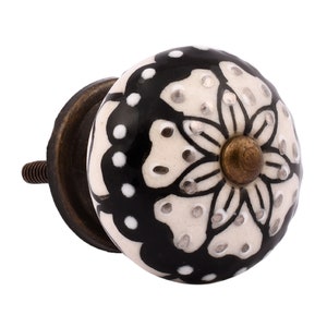 May include: A white ceramic knob with a black floral design and gold accents. The knob has a brass screw.