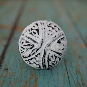 May include: A white and black ceramic knob with a detailed, intricate design. The knob is round and has a smooth, glossy finish.