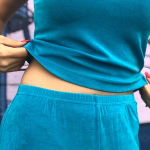 May include: A turquoise blue two-piece outfit with a short-sleeved top and pants. The top is tucked into the pants, showing the waistband.
