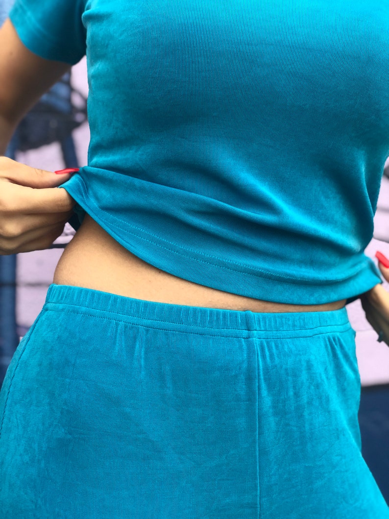 May include: A turquoise blue two-piece outfit with a short-sleeved top and pants. The top is tucked into the pants, showing the waistband.