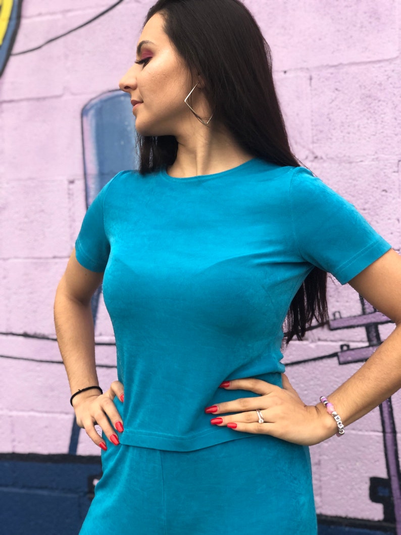 May include: A woman wearing a turquoise blue short-sleeved top and matching pants. The top has a round neckline and the pants have a wide leg.