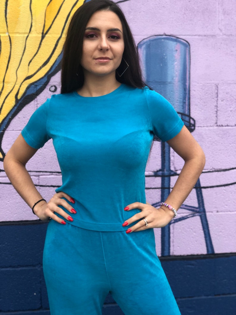May include: A turquoise blue velour jumpsuit with short sleeves and a crew neck. The jumpsuit has a relaxed fit and is made of a soft, comfortable fabric.