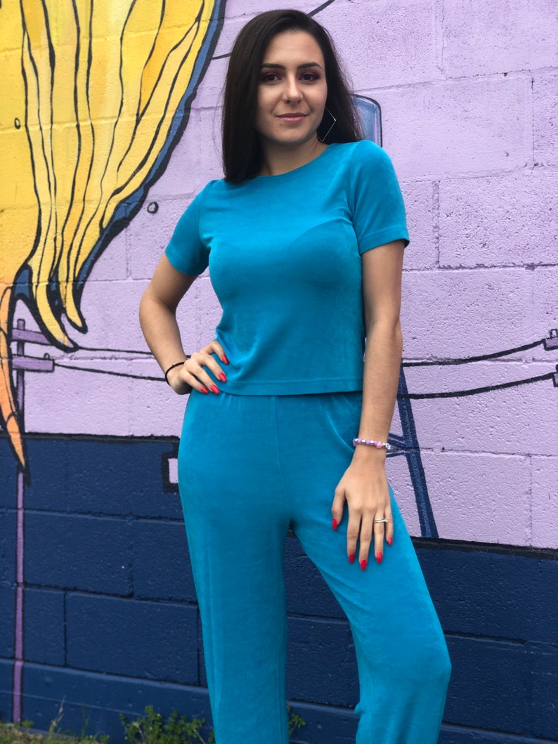 May include: A woman wearing a teal blue short-sleeved top and matching pants. The outfit is made of a soft, textured fabric.