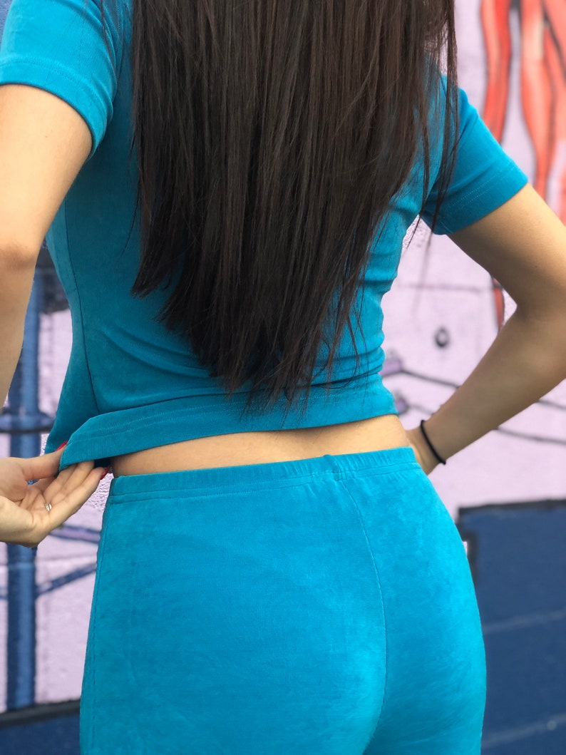 May include: A woman wearing a turquoise blue short-sleeved shirt and matching pants.
