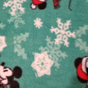 K&ouml;nnte beinhalten: Gr&uuml;ner Stoff mit einem wei&szlig;en Schneeflockenmuster und einem sich wiederholenden Bild von Mickey Mouse mit einem Weihnachtsmann-Hut.