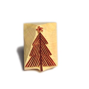 Könnte beinhalten: Ein Holzstempel mit einem roten Weihnachtsbaum-Design und Stern auf einem hellen Holzblock. Ideal für Bastelarbeiten und Weihnachtsdekorationen. Perfekt für festliche Projekte.