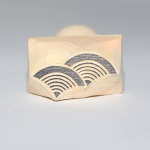 May include: A wooden stamp with a black and white design of stylized waves. The stamp is rectangular and has a rounded top.