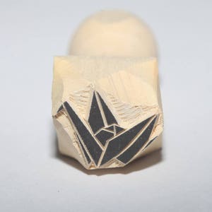 May include: A wooden block stamp with a black origami crane design. The stamp is carved with detail and ready to be used for crafting and art projects.