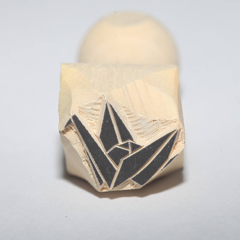 May include: A wooden block stamp with a black origami crane design. The stamp is carved with detail and ready to be used for crafting and art projects.