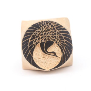 May include: A wooden block with a black and white design of a crane with its wings spread. The crane is in a circle on the block.
