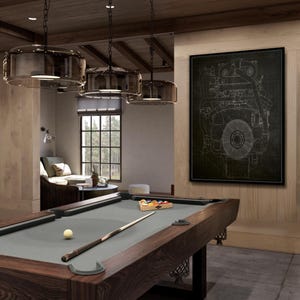 May include: A pool table with a gray felt surface and dark wood frame. A cue stick rests on the table next to a white cue ball. A rack of billiard balls is in place. Three pendant lights hang above the table.