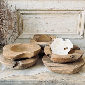 May include: A collection of rustic wooden bowls in various sizes and shapes. The bowls have a natural, unfinished look, showcasing the wood grain. One bowl contains a white, coral-like decorative piece. The bowls are arranged on a light-colored surface.