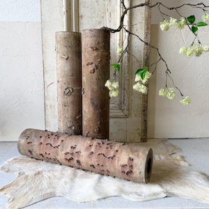 May include: Three cylindrical wooden rollers with textured, weathered surfaces featuring small, repeating carved patterns. Two rollers stand vertically while one lies horizontally in the foreground, all displaying a natural brown wood grain.