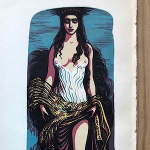 Puede incluir: Una impresión en madera de colores de una mujer con cabello largo y oscuro que lleva un vestido blanco y una túnica dorada y morada. Está de pie en una playa de arena con un cielo azul detrás de ella.