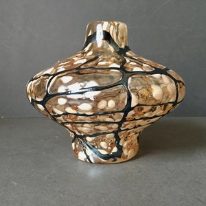 Puede incluir: Un pequeño jarrón de vidrio transparente con una base ancha y redondeada y un cuello estrecho. El jarrón está decorado con un patrón geométrico en blanco y negro.