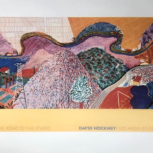 May include: A colorful landscape print titled "Mulholland Drive The Road to the Studio" by David Hockney. The artwork features rolling hills, a winding road, and power lines, with text at the bottom. The color palette includes blues, pinks, greens, and oranges.