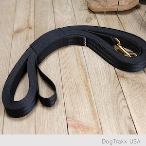 May include: Black dog leash with a gold metal clip and a red, white, and blue stripe. DogTrakx USA is printed on the leash.