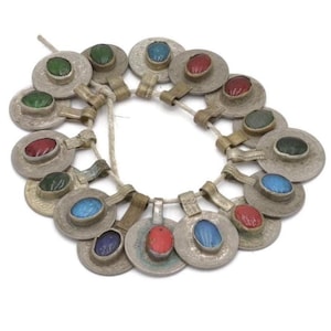 May include: A necklace featuring silver-toned, circular pendants with colorful, oval-shaped gemstones. The gemstones are in shades of red, green, and blue. The pendants are strung together with a natural-colored cord.