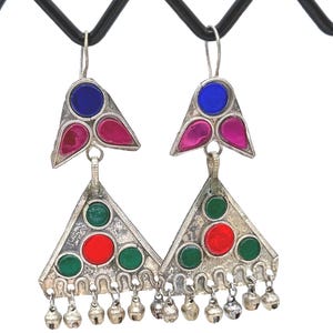 Puede incluir: Pendientes plateados con incrustaciones de vidrio de colores. Cada pendiente presenta un diseño triangular con detalles rojos, verdes y azules, y pequeñas campanillas colgantes. Estética vintage.