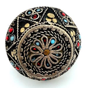 May include: A decorative, spherical object in black and silver, featuring a floral motif. It is adorned with red, blue, and gold embellishments. The silver border has a detailed, textured design.