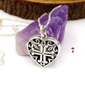 May include: A silver heart-shaped locket necklace with an intricate design. The locket is open and the inside is visible. The necklace is on a white background.